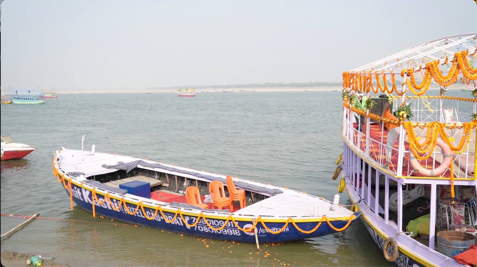 Normal wooden boat decorated with marigolds beside a larger boat on the Ganga
